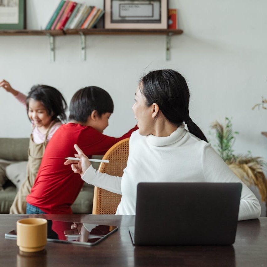 Mom working on computer while children run around in background